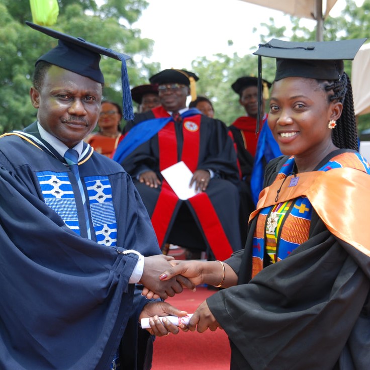 Graduation photo of a student shaking hands with a professor, accepting her diploma.